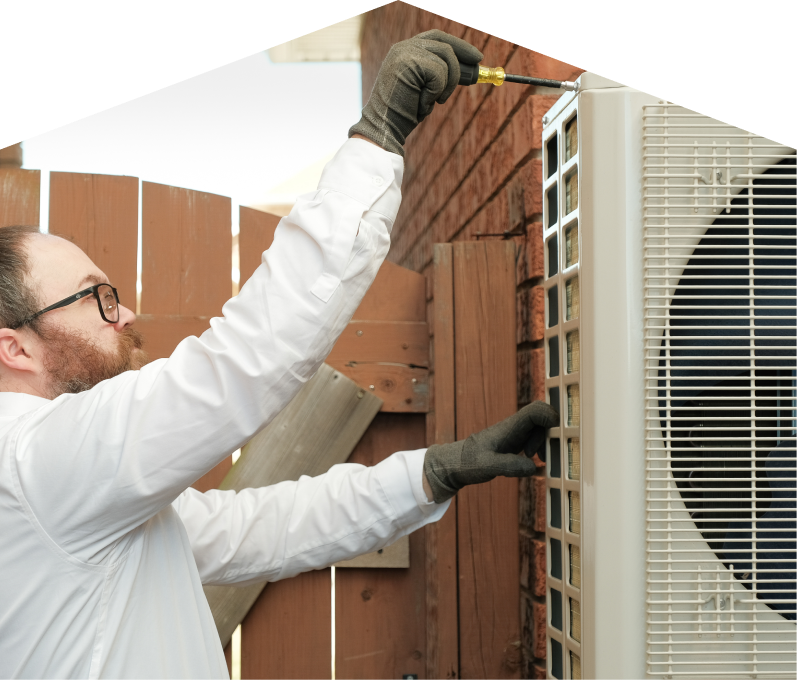 Mersey service personnel working on an AC condenser, using a screwdriver to secure the unit’s panel outdoors beside a wooden fence. Mersey service personnel working on an AC condenser, using a screwdriver to secure the unit's panel outdoors beside a wooden fence.