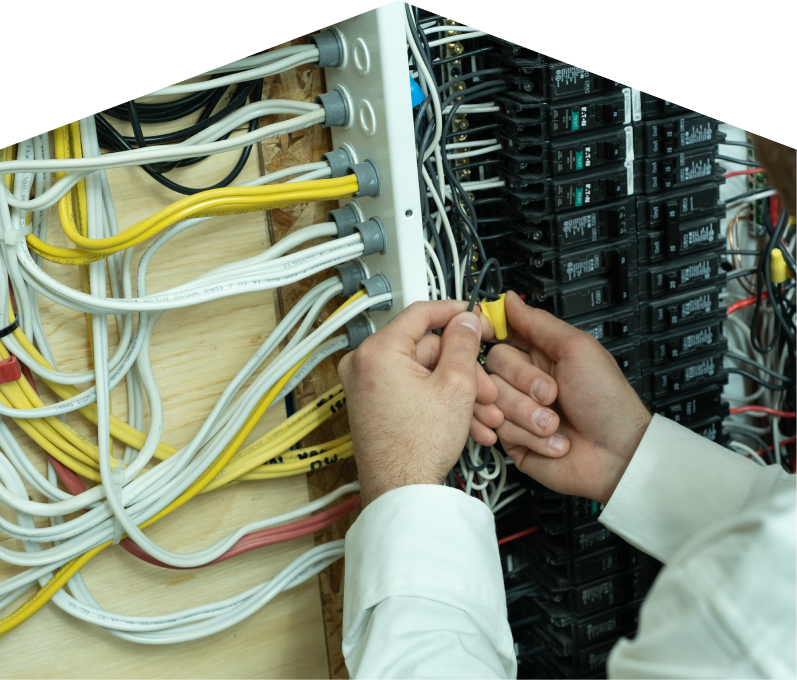 Mersey service personnel working on electrical installations, connecting wires inside a residential breaker panel with neatly arranged colored cables on a plywood backing. Mersey service personnel working on electrical installations, connecting wires inside a residential breaker panel with neatly arranged colored cables on a plywood backing.