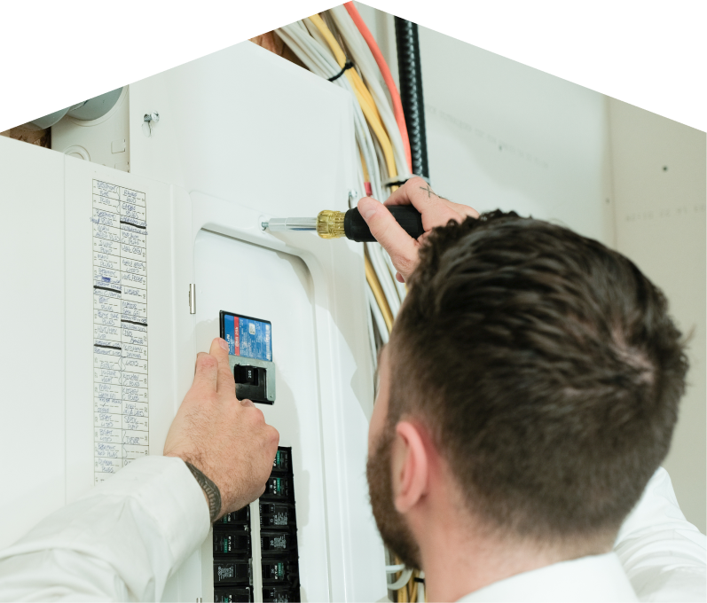 Mersey electrician using a screwdriver to perform an electrical panel upgrade, working near organized wiring in a residential wall. Mersey electrician using a screwdriver to perform an electrical panel upgrade, working near organized wiring in a residential wall.