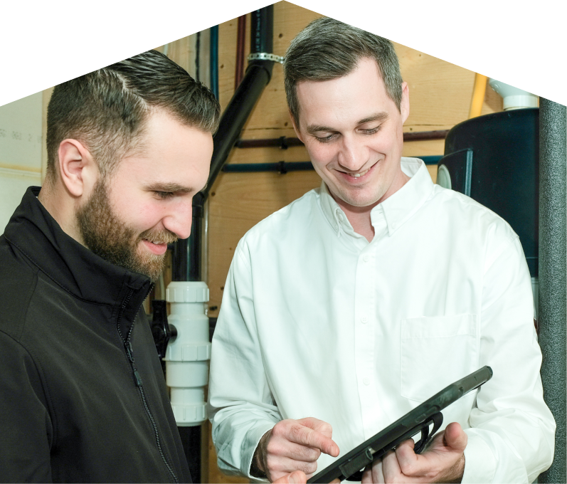 Mersey specialist reviewing maintenance plan options with a smiling homeowner using a tablet, inside a utility room with visible piping. Mersey specialist reviewing maintenance plan options with a smiling homeowner using a tablet, inside a utility room with visible piping.