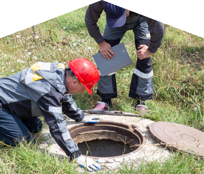 Mersey sewer crew inspecting an open manhole in a grassy field, with one member documenting findings on a clipboard. Mersey sewer crew inspecting an open manhole in a grassy field, with one member documenting findings on a clipboard.