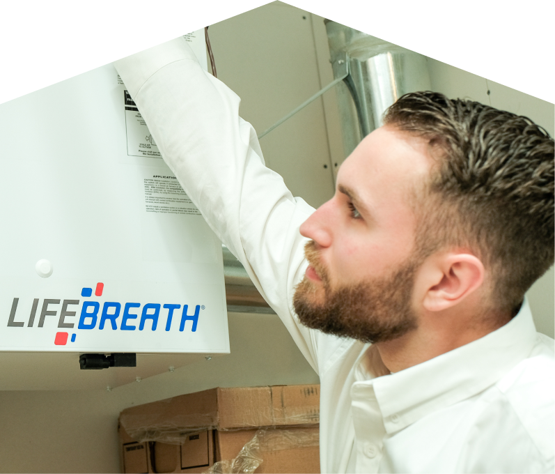 Mersey indoor air quality specialist inspects a Lifebreath ventilation unit related to UV air purifiers, with ductwork and boxes in the background. Mersey indoor air quality specialist inspects a Lifebreath ventilation unit related to UV air purifiers, with ductwork and boxes in the background.