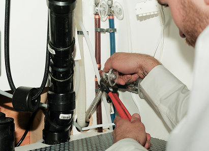 Using two pipe wrenches, a Mersey professional plumber services a pipe connection near a vertical flue or vent pipe. Using two pipe wrenches, a Mersey professional plumber services a pipe connection near a vertical flue or vent pipe.